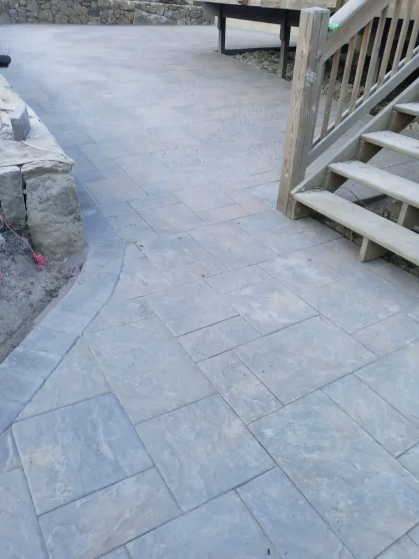 New stone patio with wooden deck stairs and railing.